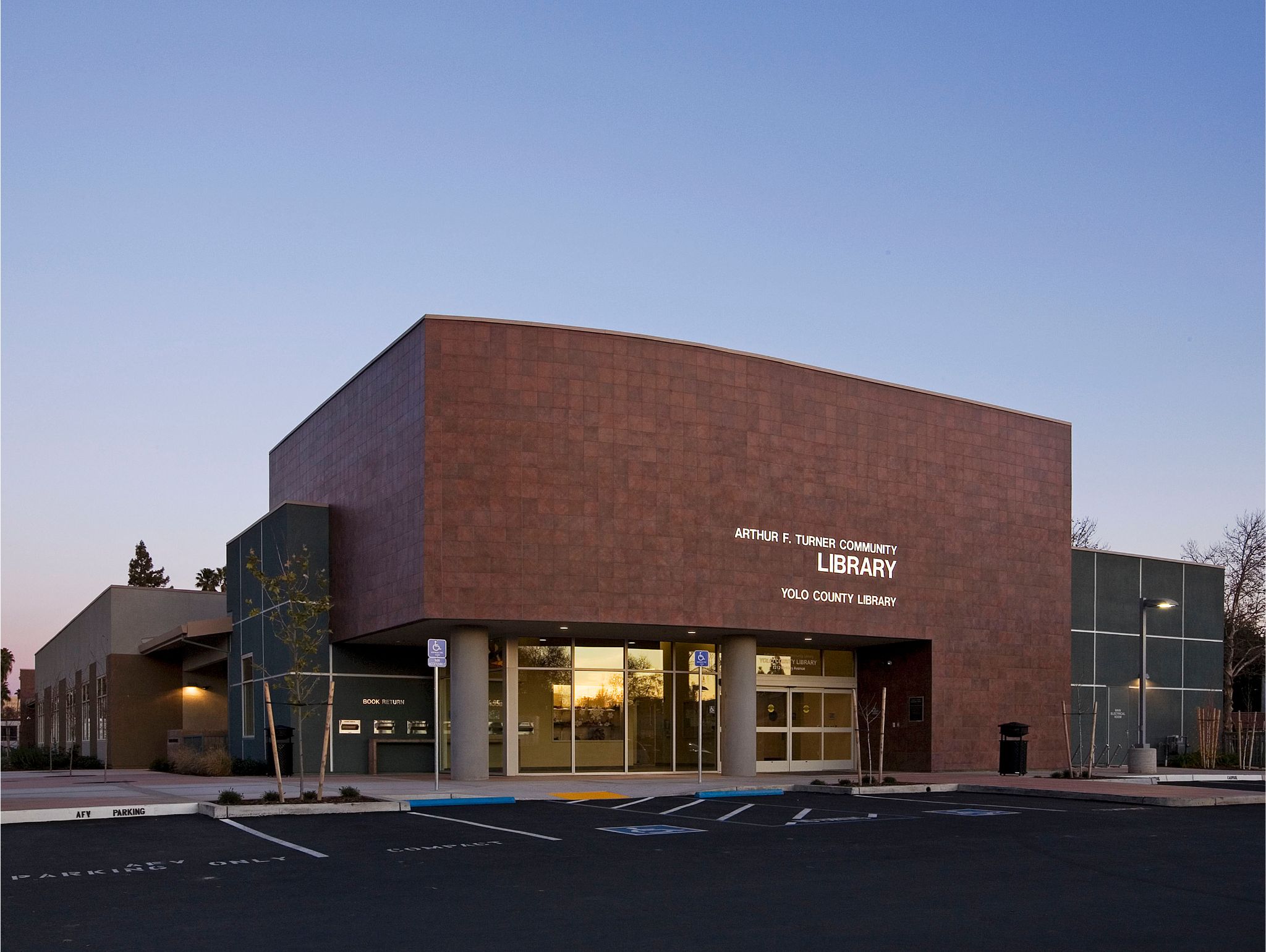 Exterior of the Arthur F. Turner Community Library in West Sacramento, featuring a brick facade, glass entrance and accessible parking spaces at dusk.