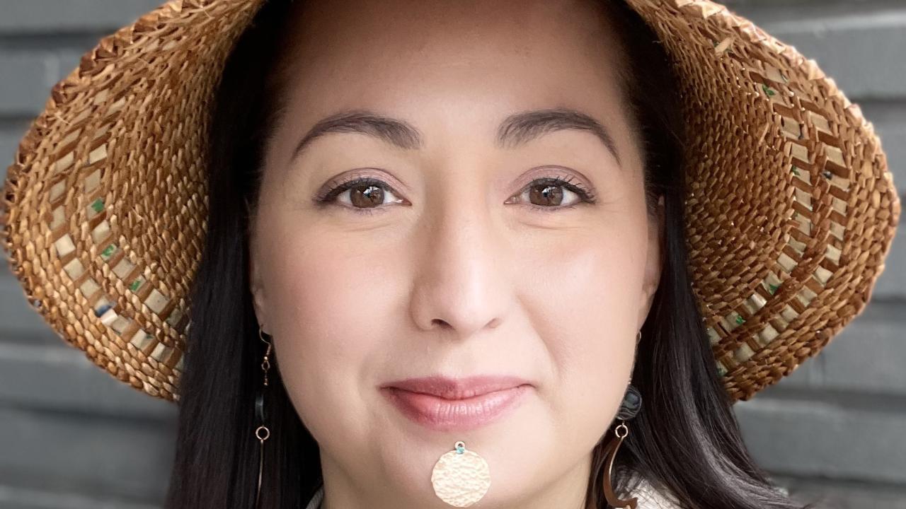 A headshot of an indigenous woman wearing a straw hat with face jewelry