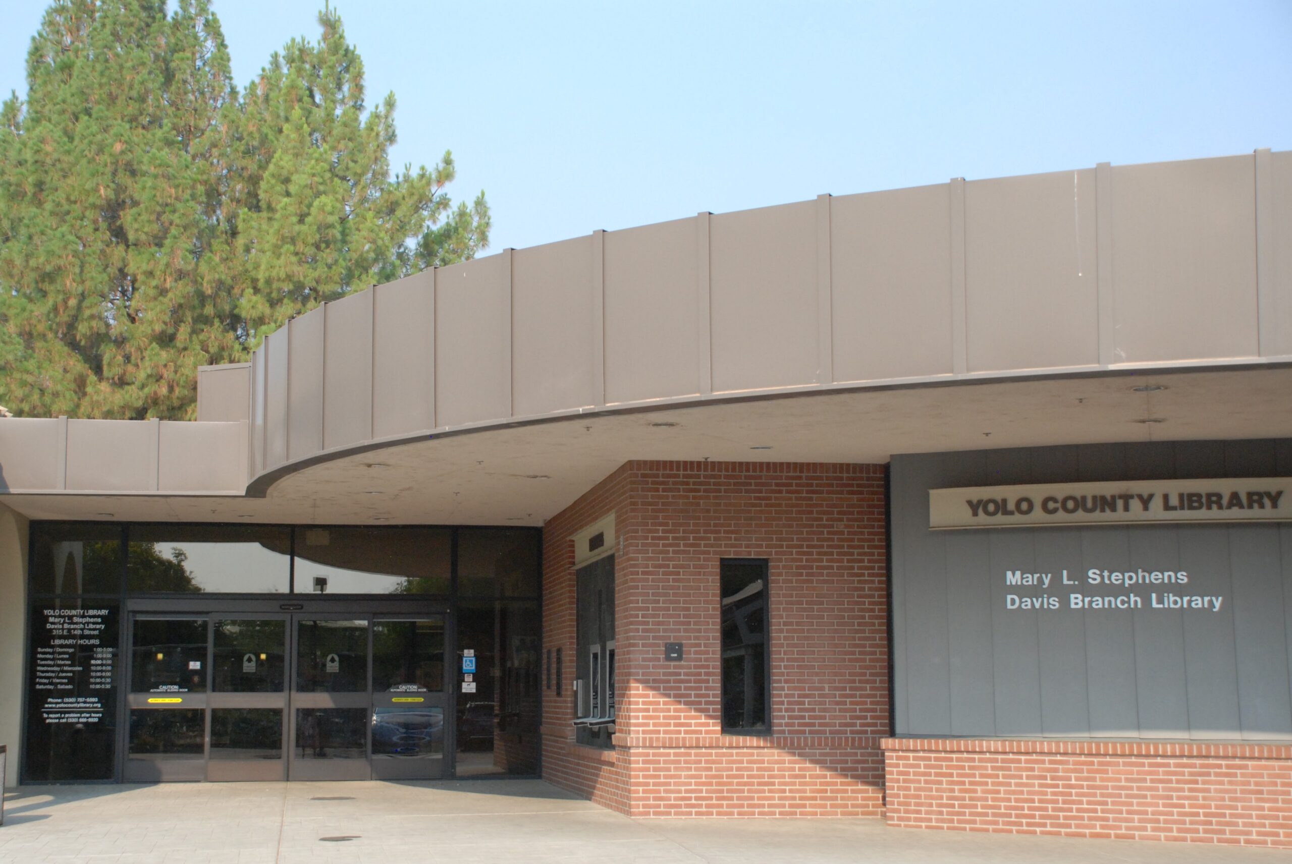 Exterior of the Mary L. Stephens Davis Branch Library in Yolo County, featuring a curved overhang, red brick walls, glass entrance doors, and signage identifying the library.