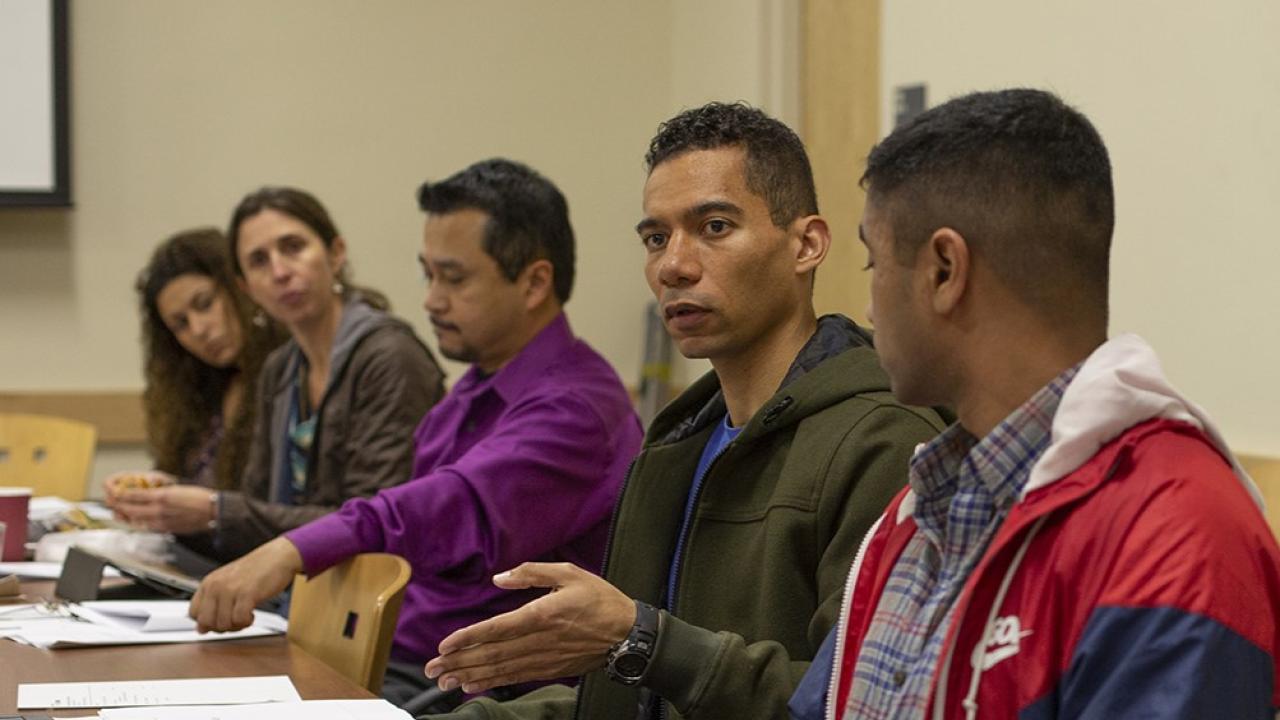 A group of students sit and talk in front of a table