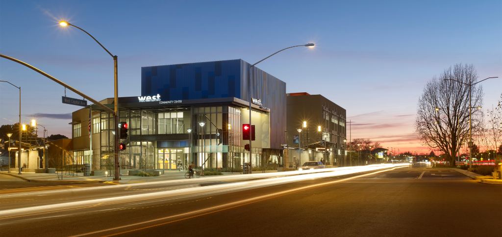 Exterior view of the West Sacramento Community Center. Street lights and stop lights are in front of the building, with a green street sign saying "West Capitol Ave."