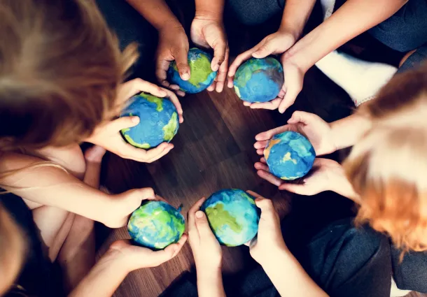 Overhead view of a group of people holding small globes in a circle, symbolizing global unity, peace, and shared responsibility for the Earth.